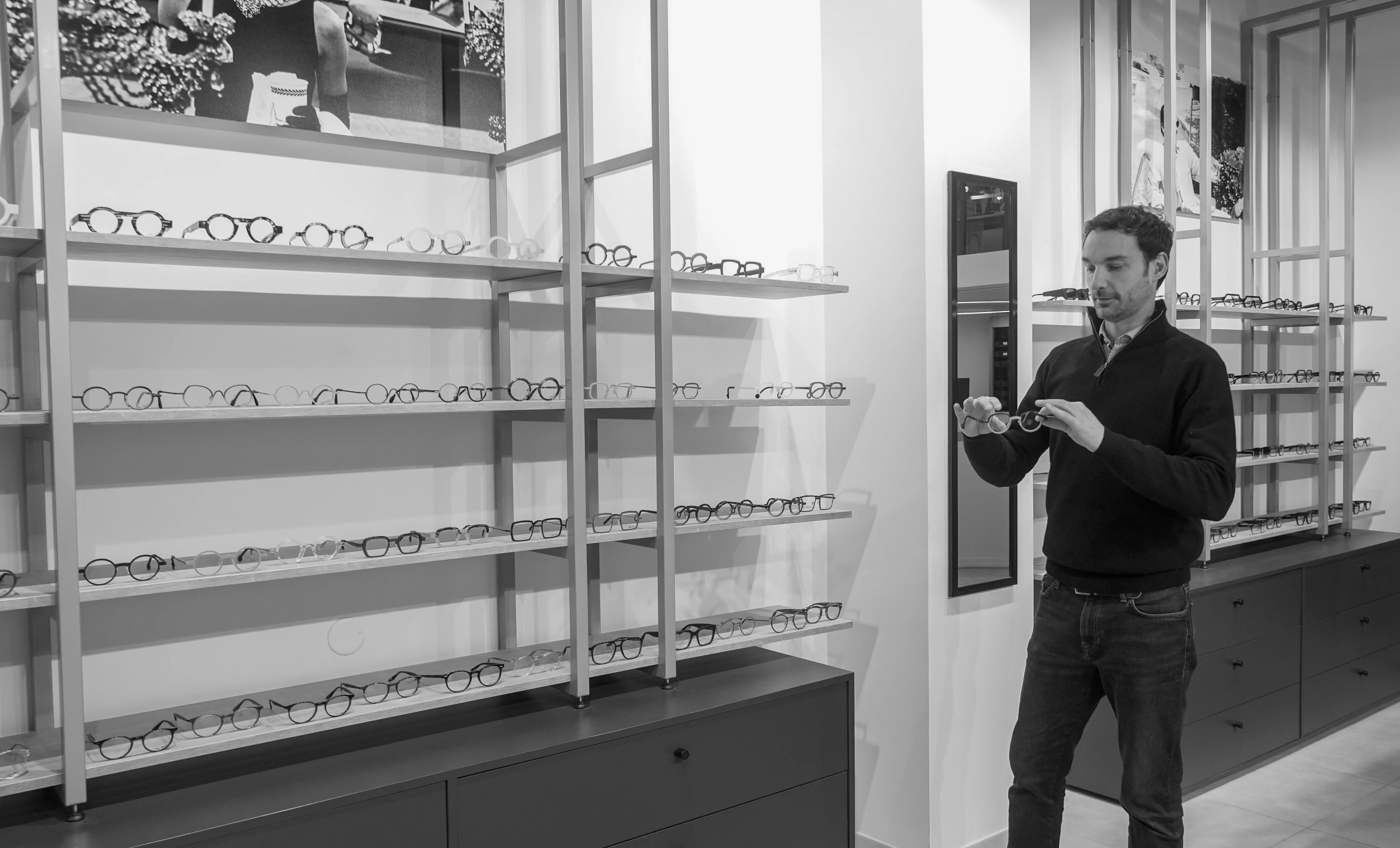 Paul-Olivier Wilpotte, opticien, examinant une monture devant les présentoirs de lunettes de sa boutique à Lille